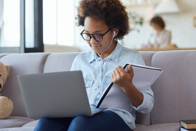 Studieren zu Hause Teen Schulmädchen mit Kopfhörern mit Laptop mit Notebook auf dem sitzen?