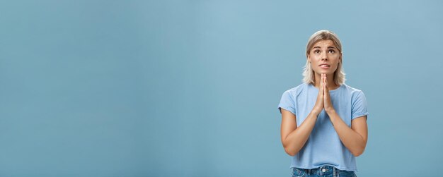 Foto studio-aufnahme eines hoffnungsvollen, fokussierten, träumenden mädchens mit attraktivem gesicht und blonden haaren, das sich die hände hält.