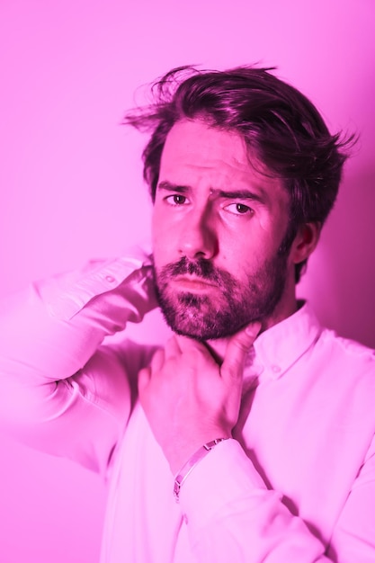 Studio-Lifestyle-Porträt eines kaukasischen Mannes mit verführerischem Blick in einem weißen Hemd, das mit einem rosa Neonlicht beleuchtet wird