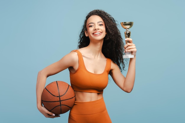 Foto studio portrait of skilled player basketball girl teenager holding ball and golden cup celebrating