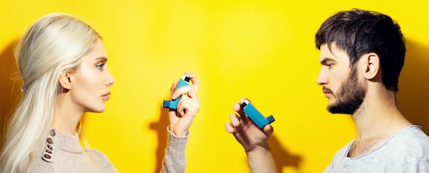 Studio-Profilporträt des Paares, des blonden Mädchens und des brünetten Kerls, die asthmatischen Inhalator auf gelbem Hintergrund halten.