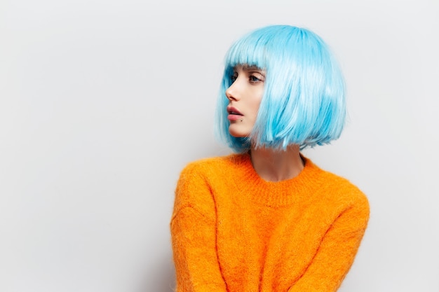 Studio-Seitenporträt des jungen Mädchens mit blauem Haar im orangefarbenen Pullover gegen weißen Hintergrund.