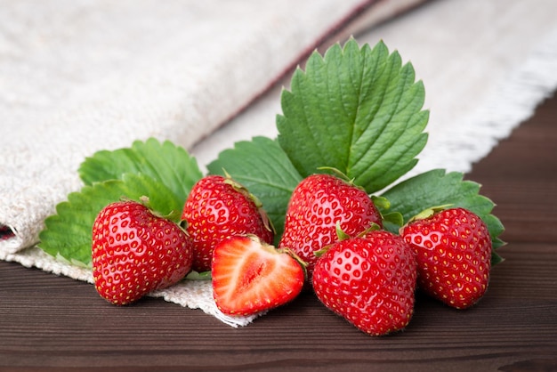 Studio-Stillleben-Foto von roten leckeren Erdbeeren auf Rindenholzhintergrund Frisch geerntete Erdbeeren auf weißem Leinentuch und dunklem Tisch