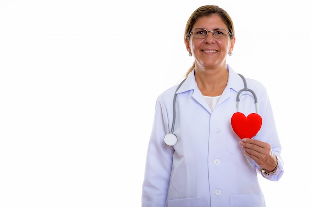Studioaufnahme der reifen glücklichen Ärztin lächelnd, während sie rotes Herz hält