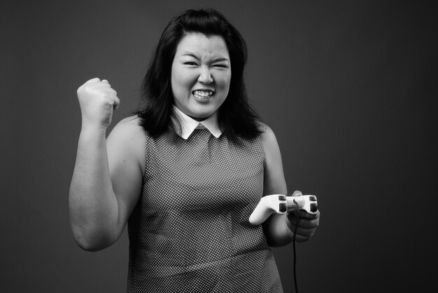 Foto studioaufnahme der schönen übergewichtigen asiatischen frau, die kleid gegen grauen hintergrund in schwarzweiss trägt