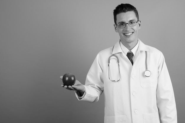 Studioaufnahme des jungen gutaussehenden Mannarztes, der Brillen gegen grauen Hintergrund in Schwarzweiss trägt