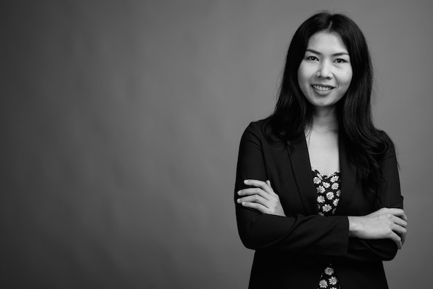 Studioaufnahme einer asiatischen Frau mit Kleid und Strickjacke vor grauem Hintergrund in Schwarz und Weiß