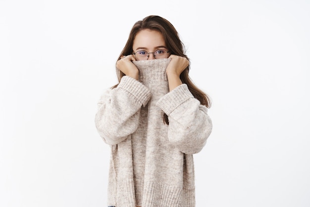 Studioaufnahme einer flirtenden und verspielten Freundin, die den Kragen des Pullovers auf die Nase zieht und mit lächelnden Augen späht