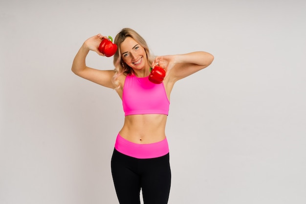 Studioaufnahme einer jungen Fitnessfrau in einer Sportkleidung mit grünem Apfel, Obst, Gemüse.