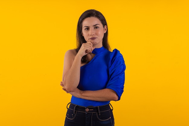 Studioaufnahme einer jungen Frau mit Brille mit blauer Bluse auf gelbem Hintergrund mit Gesichtsausdruck