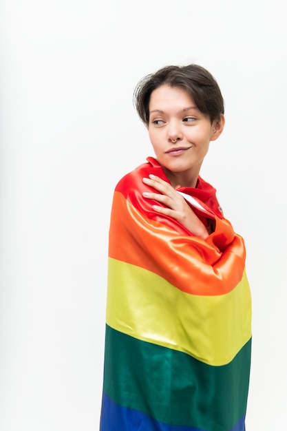 Studioaufnahme einer jungen schwulen Frau, die selbstbewusst zurückblickt und die LGBTQ-Ikonenflagge trägt