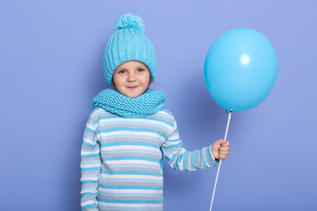 Studiofoto des kleinen Mädchens, das über blauem Hintergrund mit Luftballon aufwirft