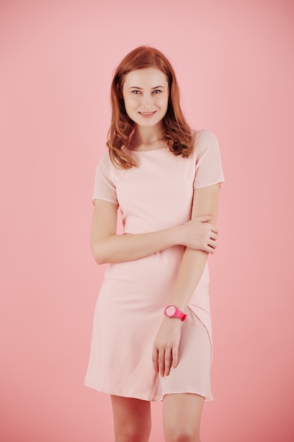 Studioporträt der glücklichen lächelnden jungen Frau im rosa Kleid, die Kamera betrachtet