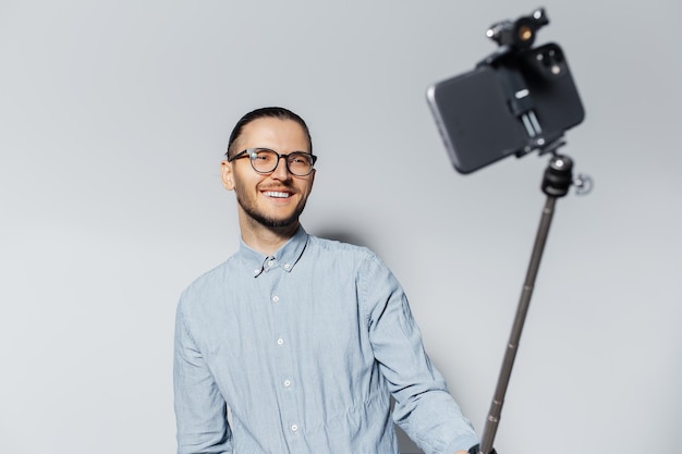 Studioporträt des jungen Glückskerls, der Foto per Smartphone mit Selfie-Stick auf weißem Hintergrund macht