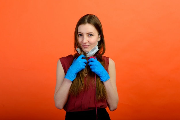 Studioporträt des jungen Mädchens, das medizinische Grippemaske und Wegwerfhandschuhe trägt, weibliches Aufstellen lokalisiert über blauer Wand. Coronavirus (COVID-19.