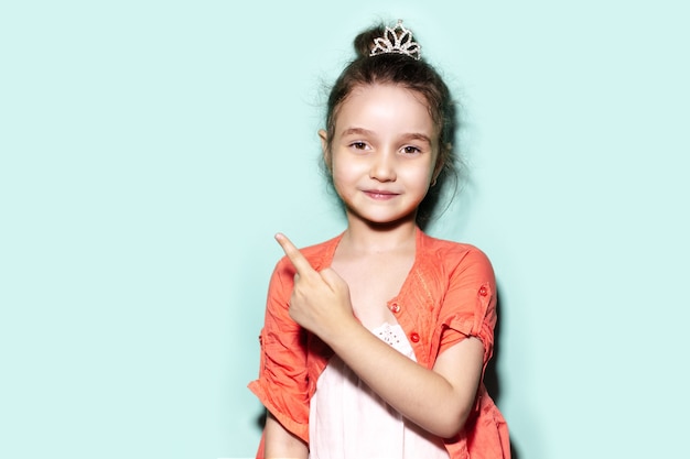 Studioporträt des lächelnden kleinen Kindermädchens, das mit dem Finger auf den leeren Hintergrund der Farbe aqua menthe mit Kopienraum zeigt
