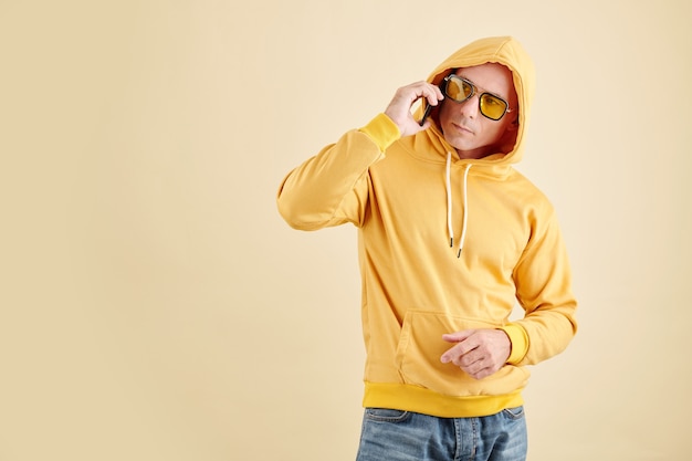 Foto studioporträt des mannes in gelbem hoodie und sonnenbrille, der mit freund telefoniert