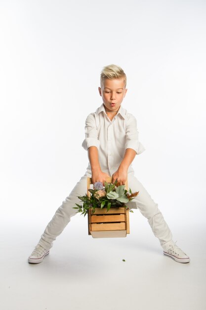 Studioporträt des modischen blonden kaukasischen Jungen mit hölzernem Blumenkorb, weißem Hintergrund, Kopienraum