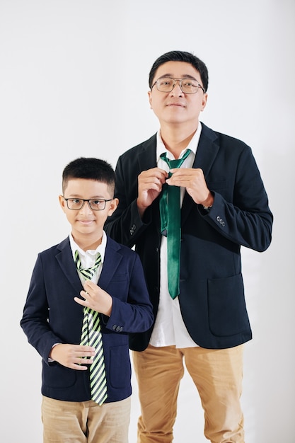 Studioporträt des positiven reifen Mannes und seines Tween-Sohnes, die Krawatten anpassen, wenn sie für Ereignis vorbereitet werden