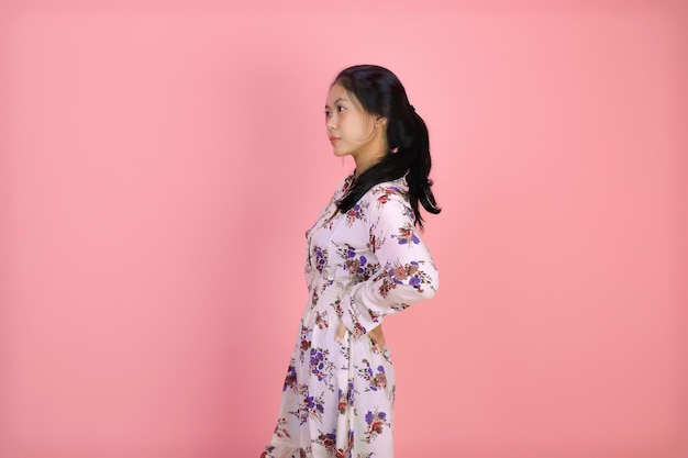 Studioporträt einer jungen asiatischen Frau mit schwarzen Haaren, die ernsthaft seitwärts auf rosa Hintergrund blickt