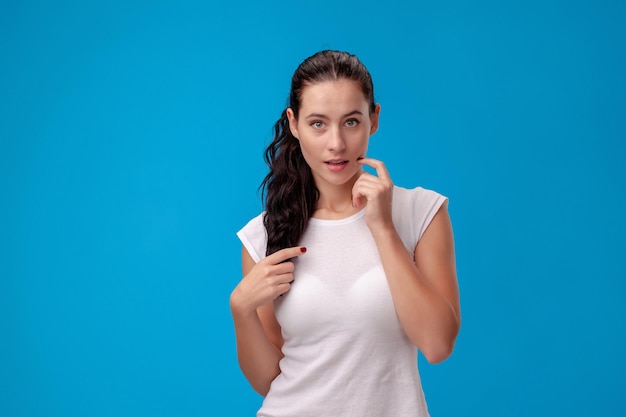 Studioporträt einer jungen schönen Frau in einem weißen T-Shirt gegen einen blauen Wandhintergrund. Menschen aufrichtige Emotionen.