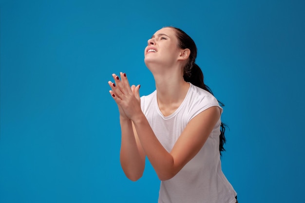 Studioporträt einer jungen schönen Frau in einem weißen T-Shirt gegen einen blauen Wandhintergrund. Menschen aufrichtige Emotionen.