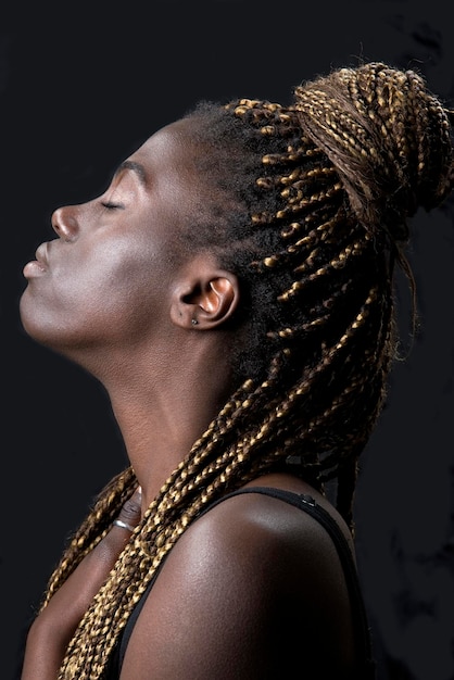 Studioporträt einer jungen schwarzen Frau mit Zöpfen und schwarzem Hintergrund