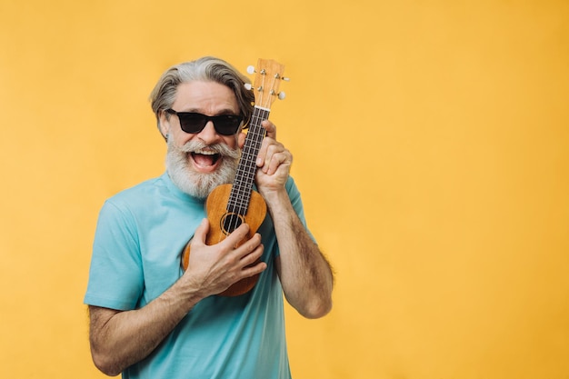 Studioporträt eines älteren Mannes mit Sonnenbrille, der eine Ukulele spielt