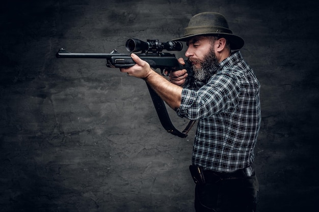 Foto studioporträt eines bärtigen jägers, der ein kariertes fleecehemd trägt, hält ein gewehr.