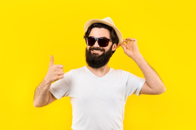 Studioporträt eines bärtigen Mannes in einem T-Shirt und einer Sonnenbrille lächelt und zeigt wie