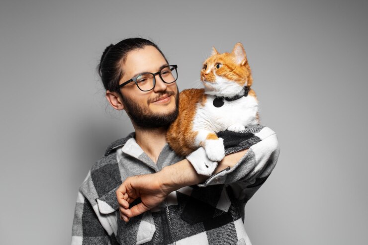 Studioporträt eines jungen lächelnden Mannes mit roter Katze auf seinen Armen Grauer Hintergrund
