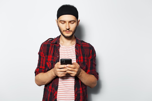 Studioporträt eines jungen mannes, der eine sms-nachricht auf dem smartphone auf weißem hintergrund trägt und ein gestreiftes hemd und ein kariertes t-shirt trägt