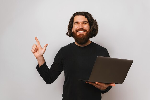 Studioporträt eines jungen Mannes, der nach oben zeigt, während er geöffneten Laptop hält