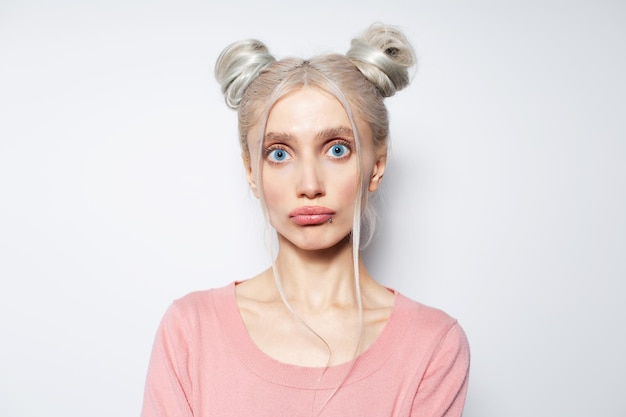 Studioporträt eines süßen blonden Mädchens mit lustigen Gesichtshaarbrötchen und blauen Augen