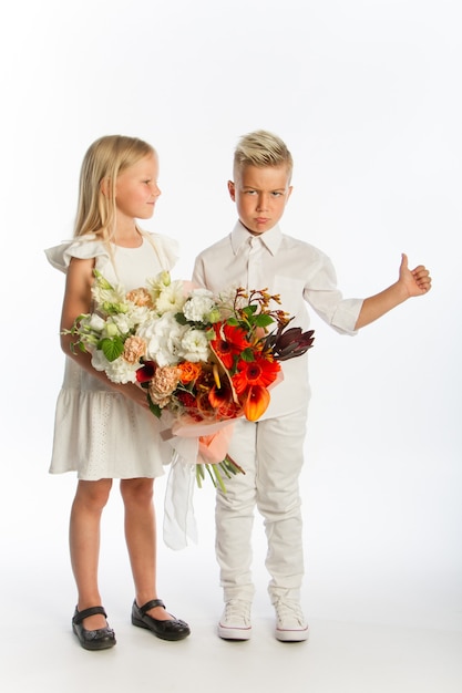 Studioporträtjunge gibt Mädchen festlichen Blumenstrauß, Glückwunschkonzept, weiße Wand, Kopienraum