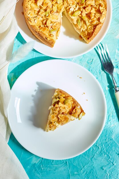 Stück Apfel- oder Birnenkuchen, Torte mit Karamellnüssen auf blauem Tisch mit Sonnenlicht