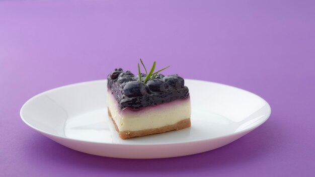 Stück Blaubeerkäsekuchen auf weißem Teller auf violettem Hintergrund