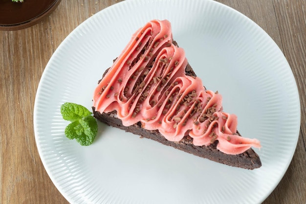 Stück Chocolate Brownie Slice mit Erdbeer- und Schokoladenglasur Holztisch mit Minze und Schokoladenstückchen im Hintergrund Ansicht von oben
