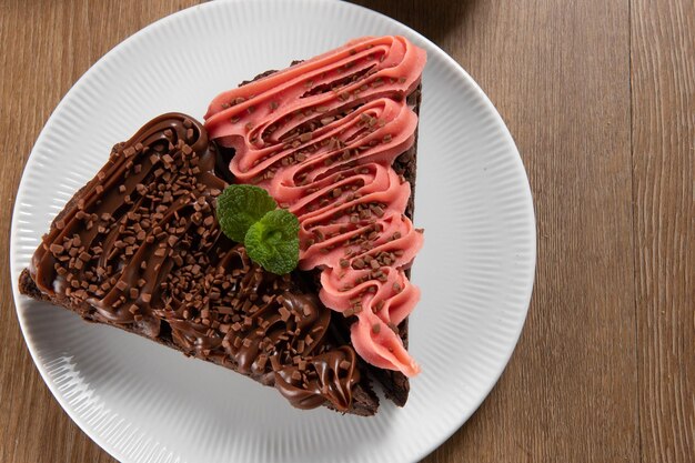 Stück Chocolate Brownie Slice mit Erdbeer- und Schokoladenglasur Holztisch mit Minze und Schokoladenstückchen im Hintergrund Ansicht von oben