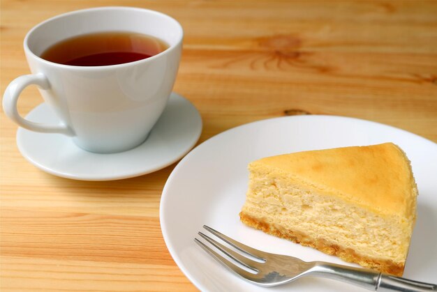 Stück gebackener Käsekuchen mit einer Tasse heißem Tee auf Holztisch serviert