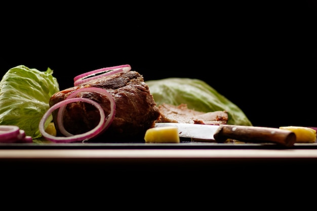 Stück gebackenes Fleisch mit Gemüse und Ananas liegen an Bord auf schwarzem Hintergrund