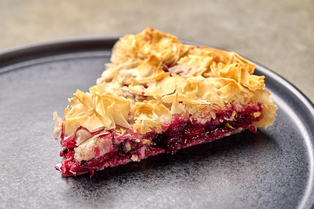 Stück hausgemachter Kirschkuchen aus Filo-Teig auf dunklem Teller, selektiver Fokus, Nahaufnahme