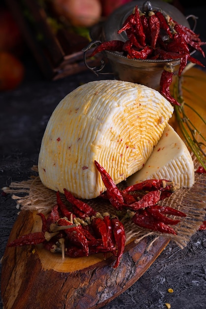 Stück italienischer Caciotta-Käse mit scharfer Chilischote auf rustikalem Holzschneidebrett