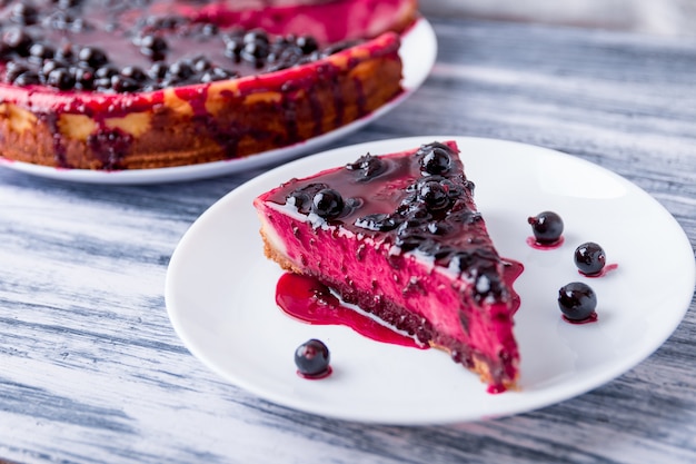 Stück käsekuchen auf weißer platte mit johannisbeere auf farbigem hölzernem.