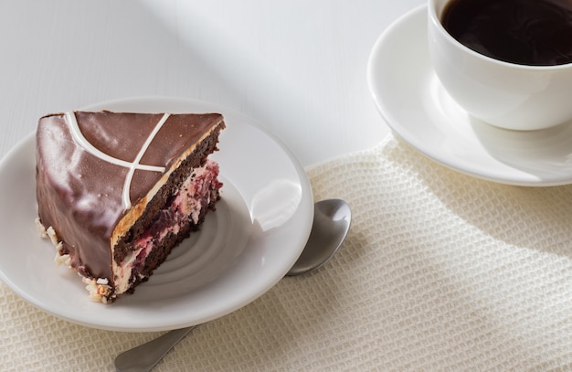 Stück köstlichen Schokoladenkuchens mit Erdbeere auf weißem Teller mit Tasse Kaffee.