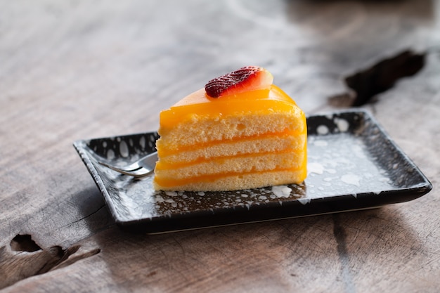 Stück köstlicher orange Kuchen auf hölzernem Schreibtisch