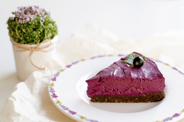 Stück Kuchen mit Sahne und Früchten. Schwarzer Johannisbeerkuchen. Lebensmittelfoto auf einem weißen Hintergrund. Hoher Schlüssel. Beeren und Blumen. Rohe Desserts.