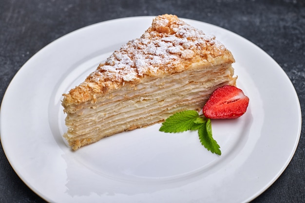 Stück Kuchen Napoleon, auf einem weißen Teller, vor einem dunklen Hintergrund