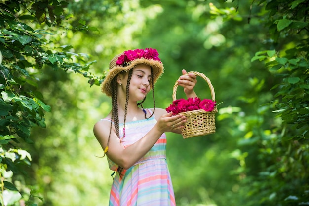 Stück Natur atemberaubendes Mädchen mit Blumenstrauß Rosen glückliches Kind im Strohhut Frisur der Natur Muttertag glücklicher Frauentag Porträt des kleinen Kindes mit Blumen Liebe und Schönheit