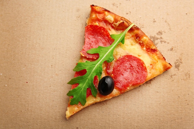 Stück Peperoni-Pizza mit Rucola und Oliven auf Karton